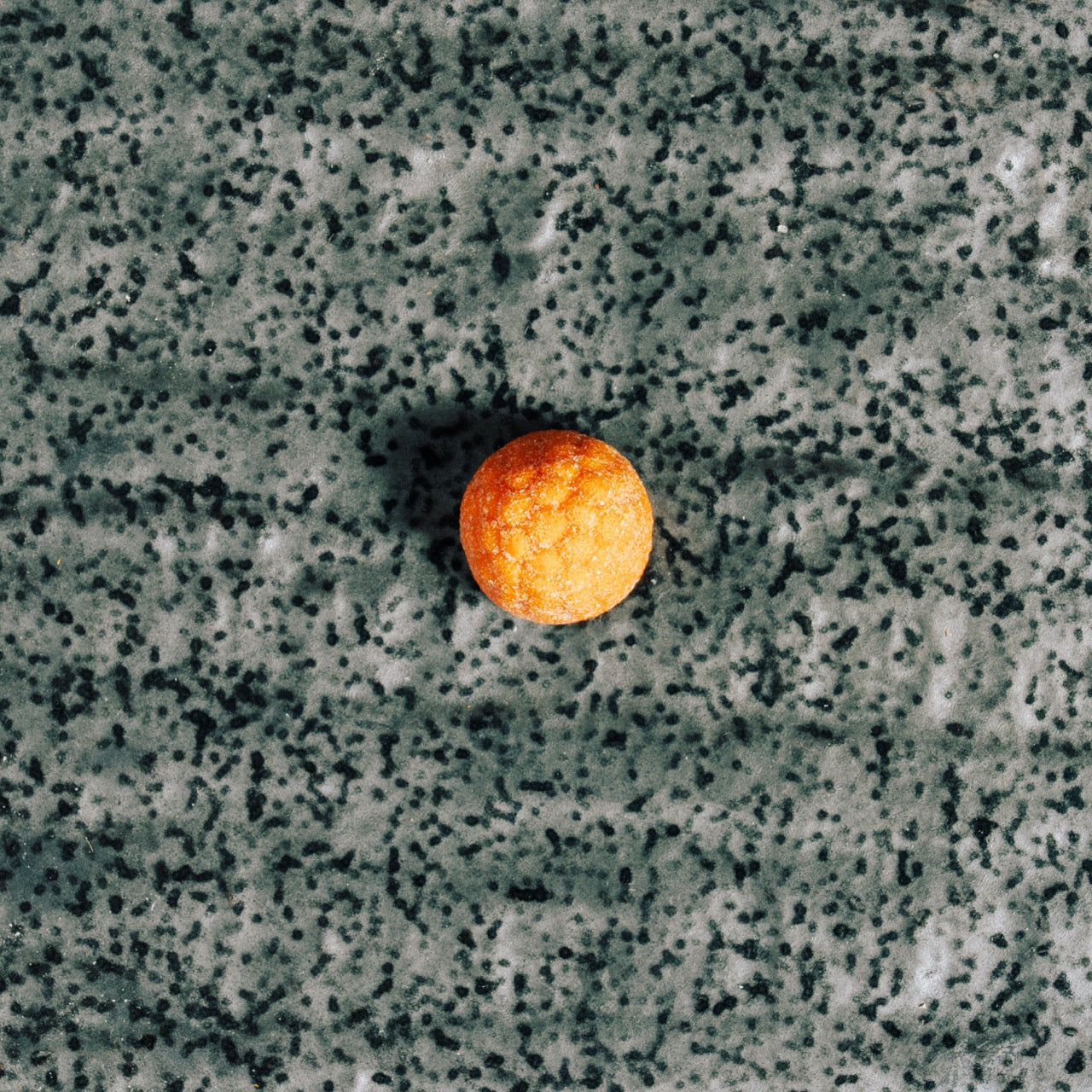 Single orange gummy on a textured gray surface