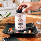 Bottle of ELK Wellness Creatine Gummies on a tray with a hand reaching for it, on a wooden surface.