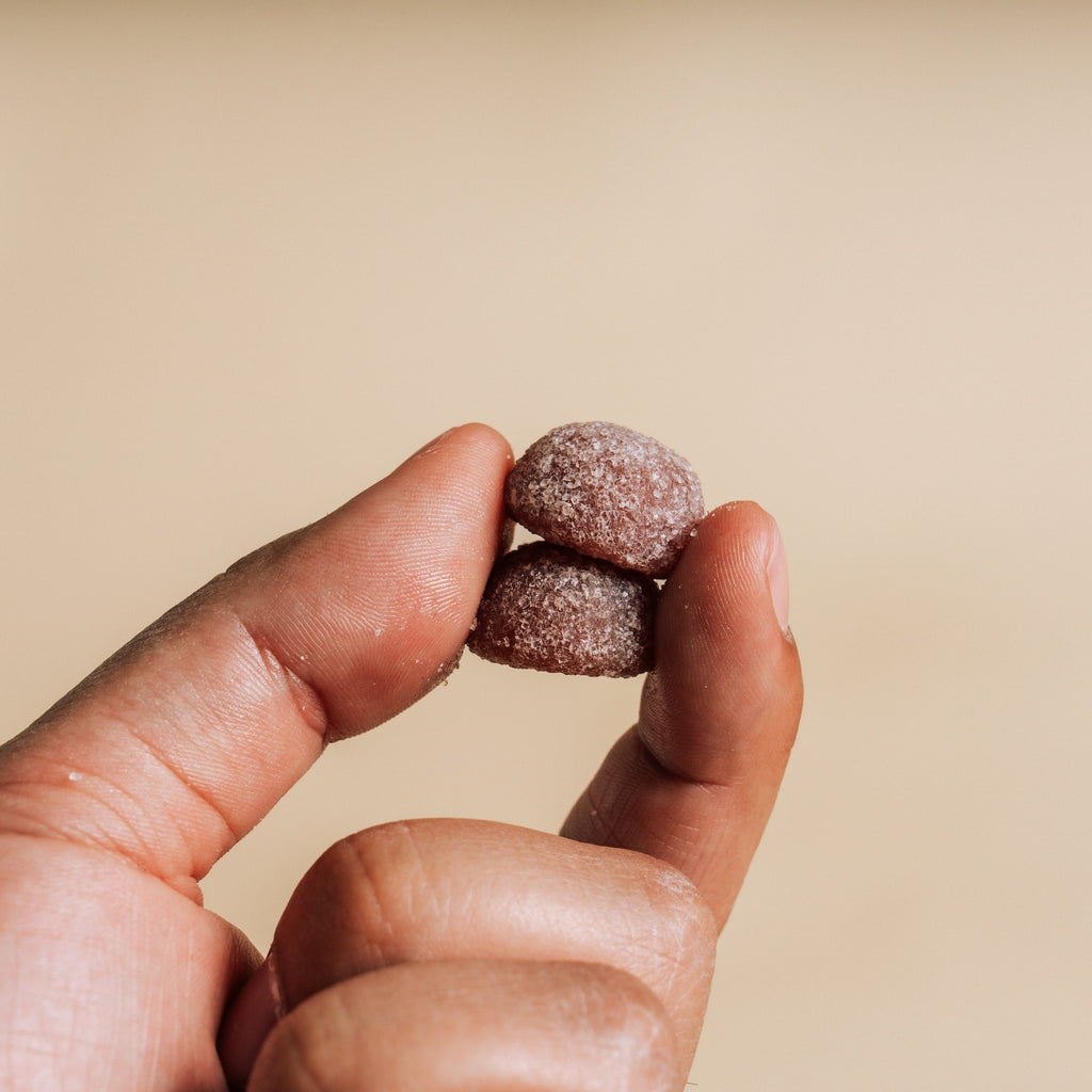 Hand holding two small, round, Gummies against a beige background