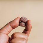 Hand holding two small, round, Gummies against a beige background