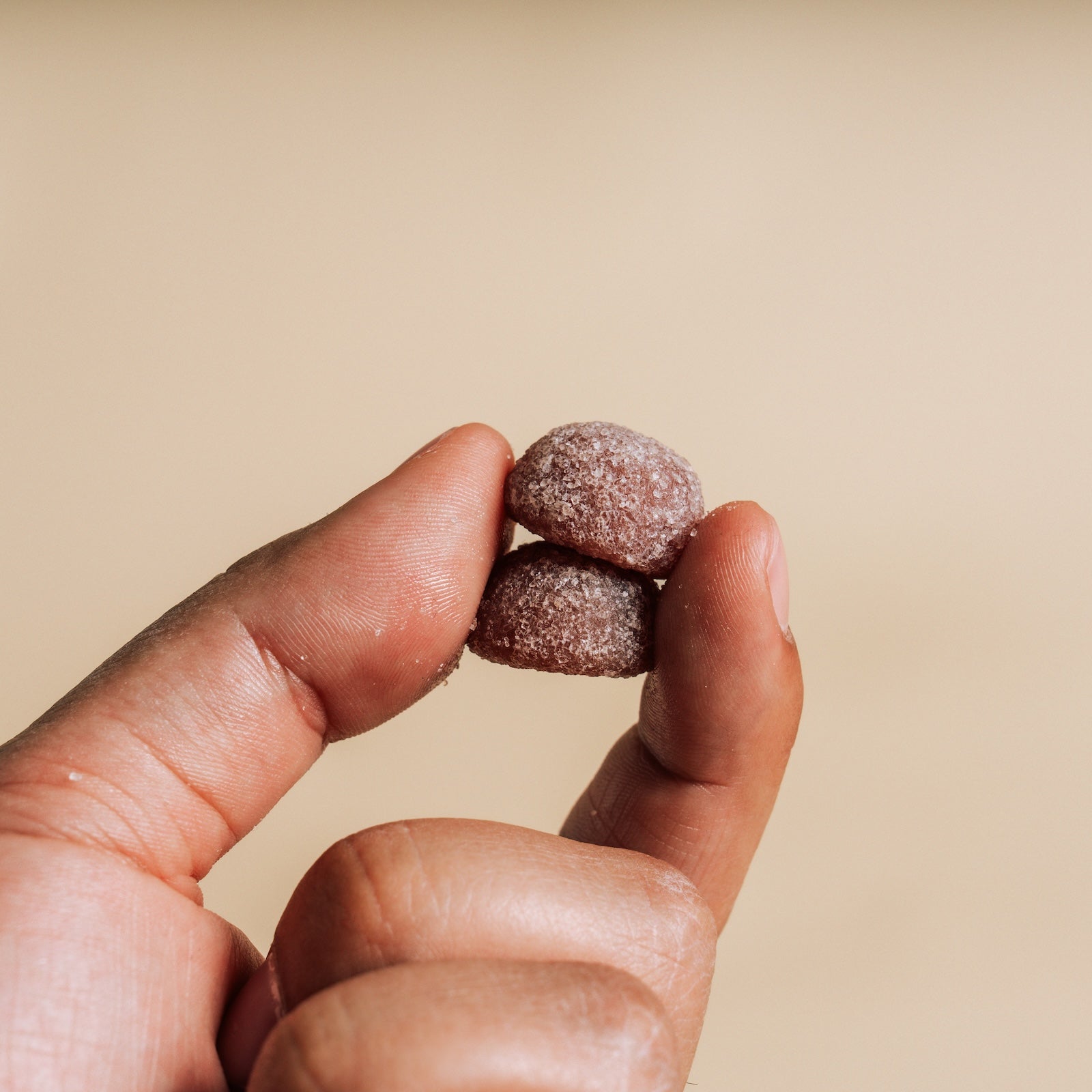 Hand holding two small, round, Gummies against a beige background